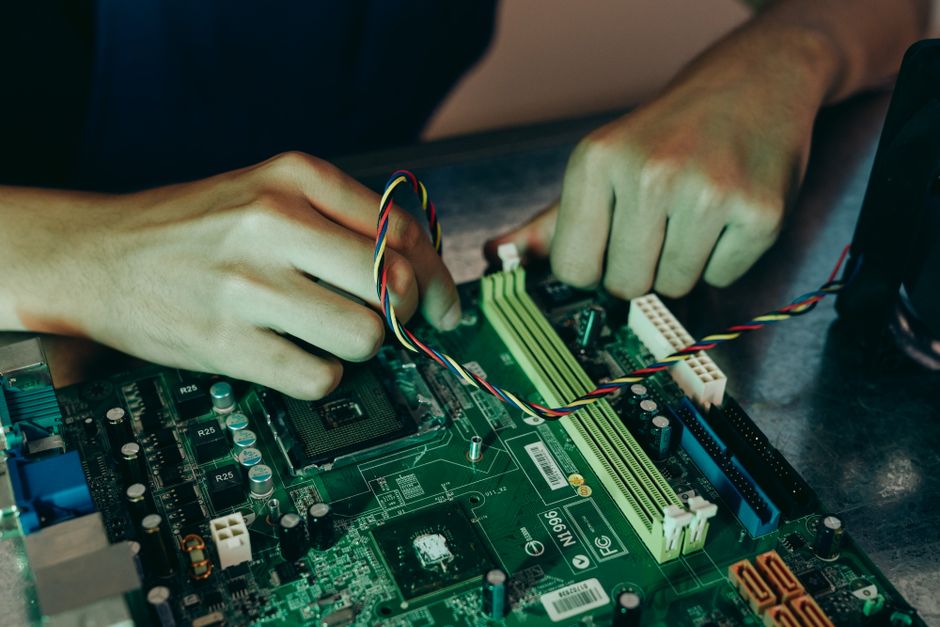 Person assembling computer motherboard with colorful wires, showcasing technology and engineering